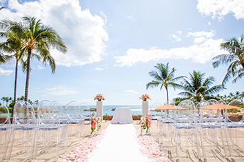 The ‘AMA ‘AMA Patio at Aulani Resort dressed for a wedding ceremony with chairs on either side of a flower lined aisle that leads to an altar with the ocean in the distance