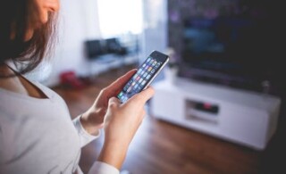 A woman in a grey shirt turns on the television with her smart phone.