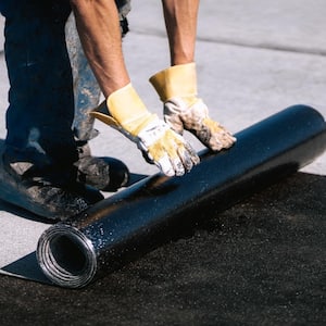 A man installing roll roofing