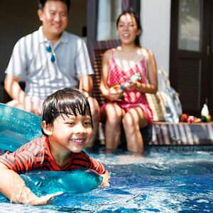 A kid in a swimming pool with his parents overlooking