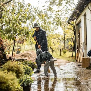 A father sweeping water from patio with two young children