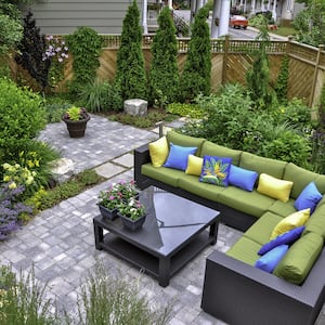 green and brown patio furniture on a stone patio area surrounded by flowers and bushes