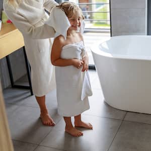 child in white towel gets hair dried by adult in bathroom with gray tiled floors and white bathtub