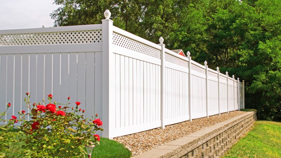 White vinyl fence in backyard with nice landscaping in the foreground and background