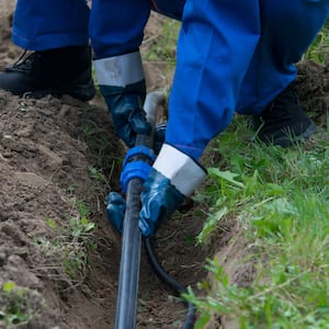 hands of the worker, in blue gloves, laid a plastic pipeline in an open trench in the ground