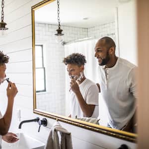 Father and son shaving in front of bathroom mirror