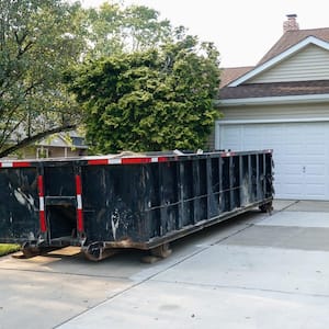 A big black dumpster in the driveway of a house