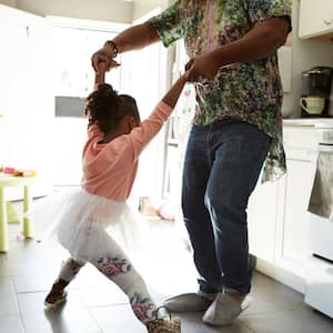 A father and his daughter dancing in a floor tiled kitchen