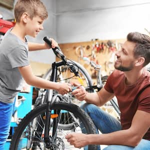 A father and son fixing bicycles in a garage with bright overhead lighting