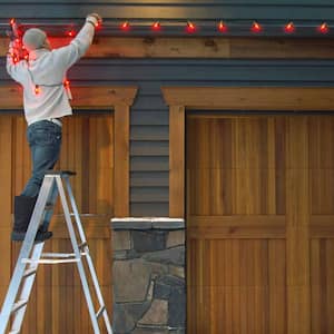 A man hanging a Christmas string of lights