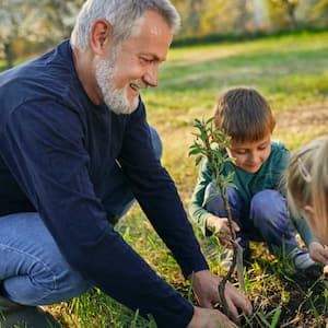 man planting tree with grandchildren at garden