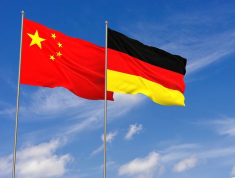 THE FLAGS OF CHINA AND GERMANY FLY ON ADJACENT POLES AGAINST A BLUE SKY