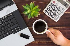 Photo of a laptop computer, cup of coffee, plant and calculator on a desk.