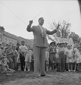 A man in a suit holds up his baton while a group of mostly children crowds together behind him. All are facing the camera.