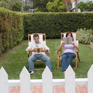 A man and woman sitting in lounge chairs in a backyard surrounded by tall privet hedges