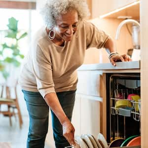 A smiling woman keeping plates in dishwasher