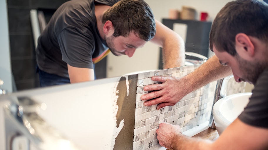Tile contractor installs square tiles under bathroom mirror