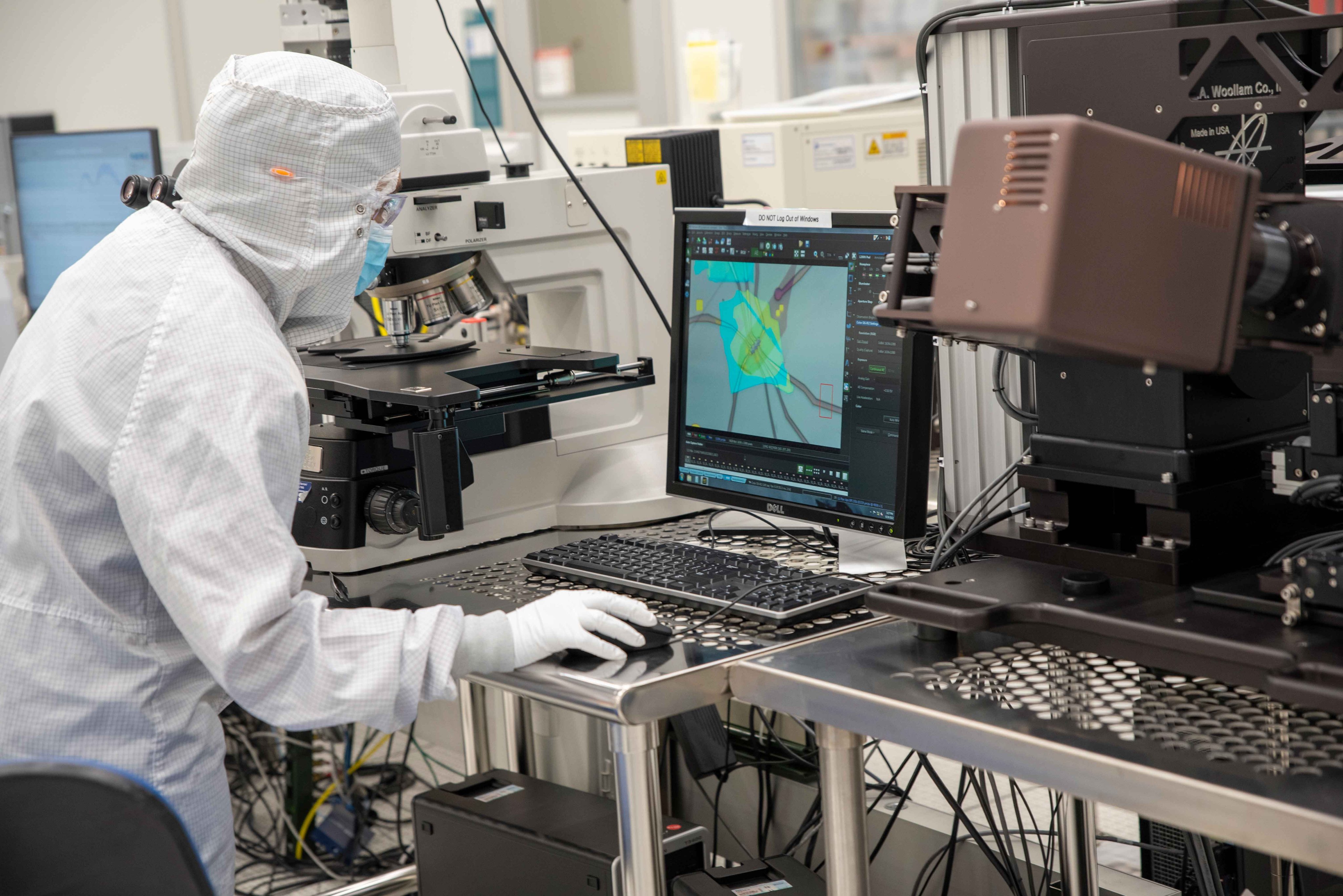 A worker in coveralls peers at a colorful computer screen next to a complicated piece of technical equipment. 