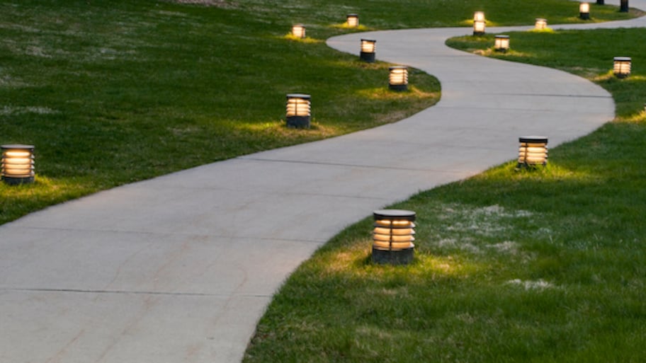 a winding concrete walkway surrounded by grass and lined with lanterns