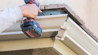 A man drills a gutter into the fascia board of a house 