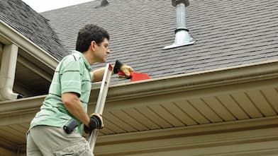 man on ladder cleaning gutter