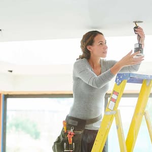 Female electrician on a ladder installing a ceiling light