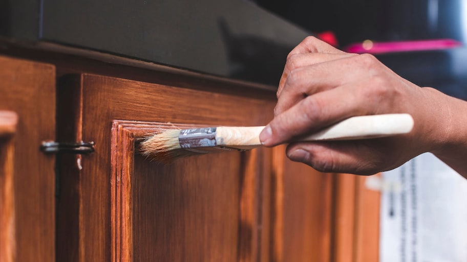 man painting on stain on wood cabinets