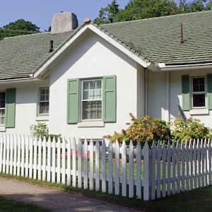 A cottage house with a green roof and a white picket fence