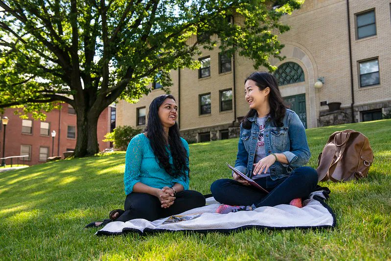 Two students sitting on the grass outside laughing