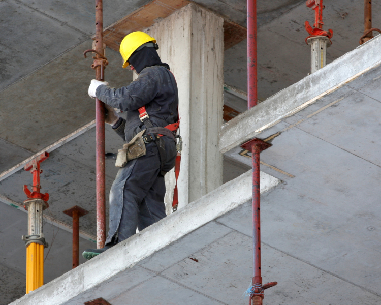 A construction worker in insulated coveralls and work gloves installing a support beam in a concrete structure