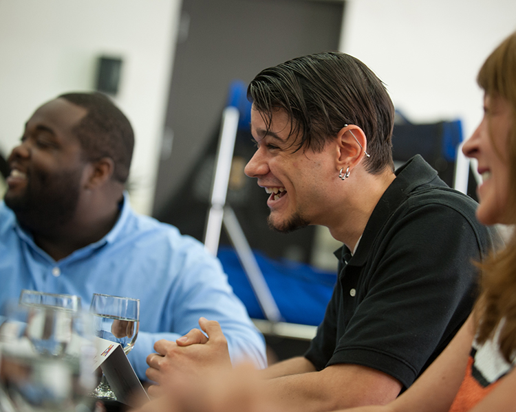 Two men and one woman seated at a table, at a safety training, laughing at a joke from the presenter.. 