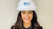 A young woman wearing a hardhat with the OSHA logo smiles at the camera.