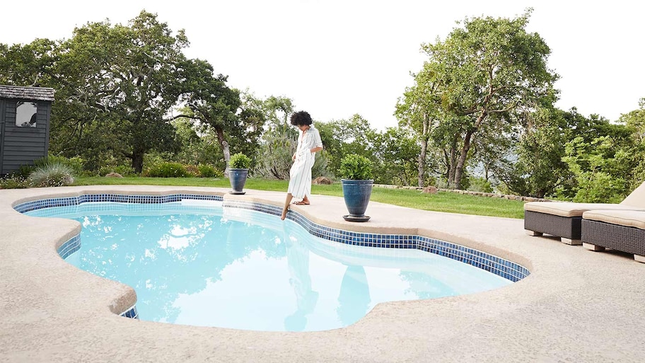 Woman dipping toes in backyard pool