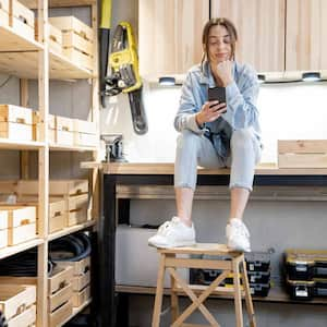 A woman sitting on her workbench in a garage with wooden shelves