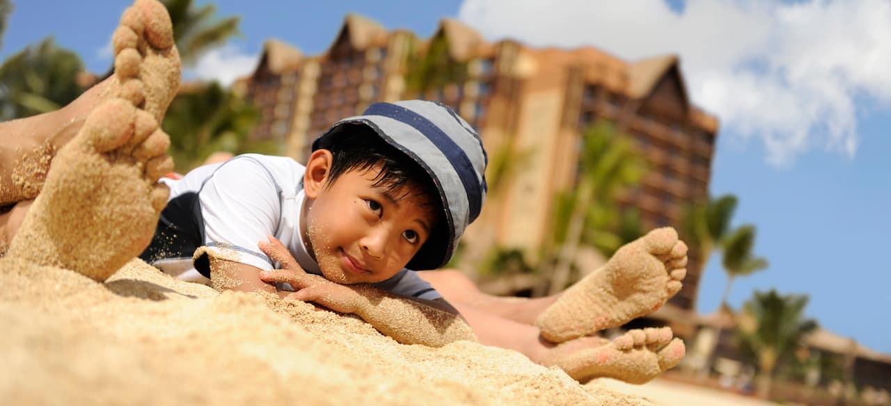 A boy lies on the sand, daydreaming between 2 pairs of sandy feet