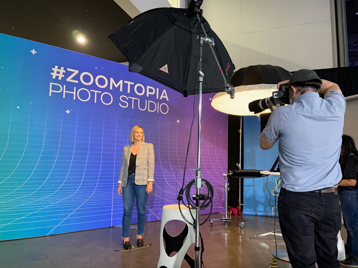 A woman wearing a smart casual outfit; with a blazer, denim jeans, and a black top, getting her headshot image taken.