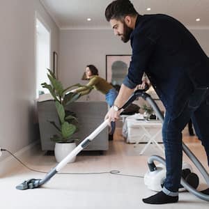 Man vacuuming floor while woman is cleaning the living room