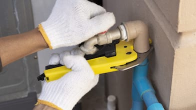 gloved hands holding pipe cutter against pipe