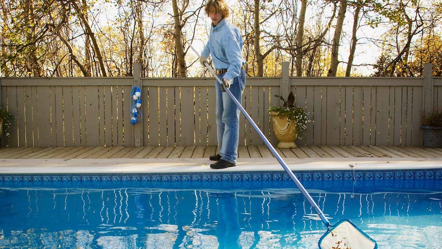 Man cleans fall leaves from pool