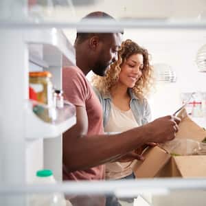 View looking out from inside of refrigerator as couple unpack groceries