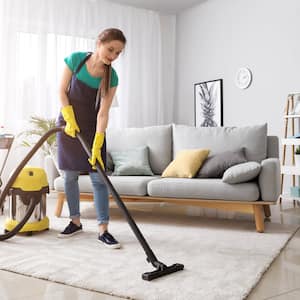 A female janitor vacuums a living room