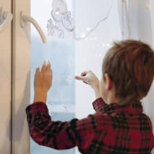 A kid decorating a window with Christmas stickers