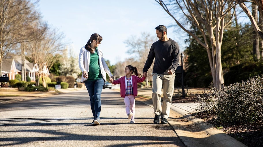 A family of three walking down a street in their neighborhood