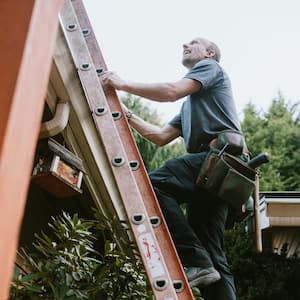 A contractor on a ladder checking a house’s roof