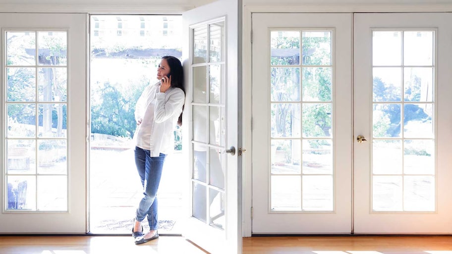 Woman using her phone standing in front of a french door