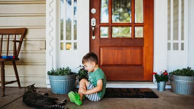 Little boy playing with cat on front porch