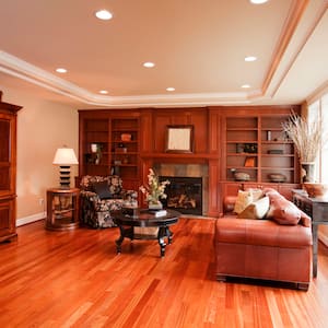 a cozy den with red hued wood floor and wooden furniture, leather couch, and recessed lights in the ceiling