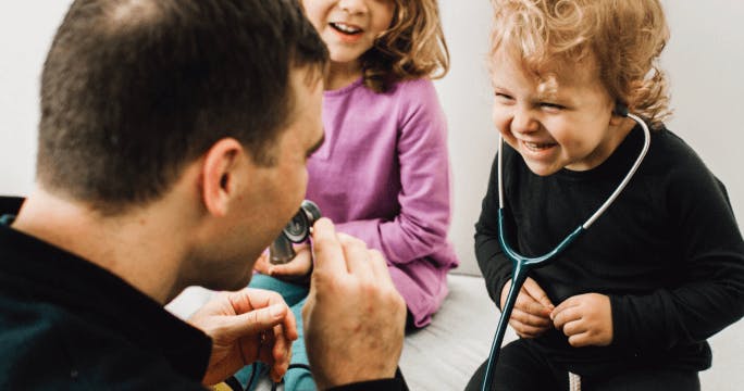 Child wearing a stethoscope laughs while doctor speaks into the other end