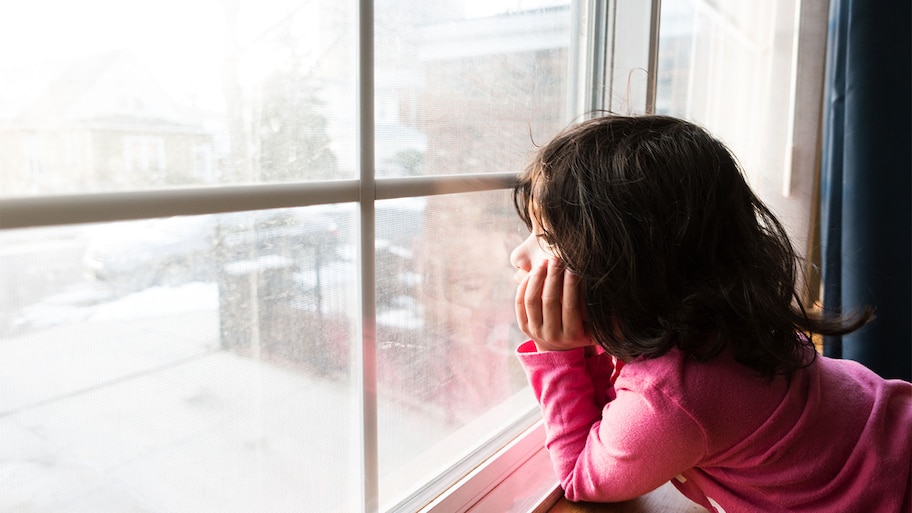 A child looks at snow outside window