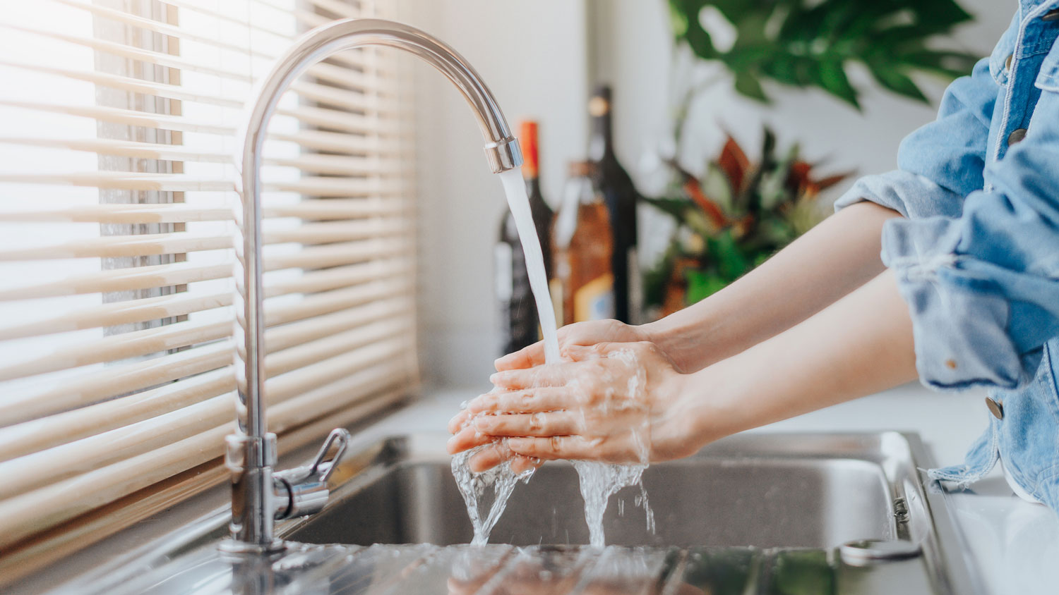 A woman testing the water temperature of the kitchen sink